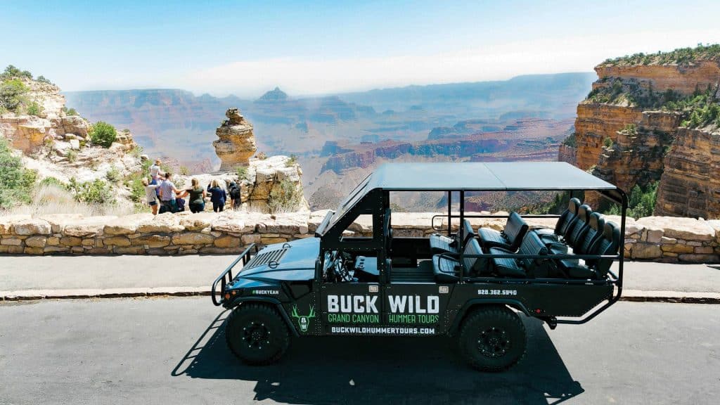 A black Buck Wild open-air safari tour vehicle parked at a Grand Canyon overlook with tourists in the background