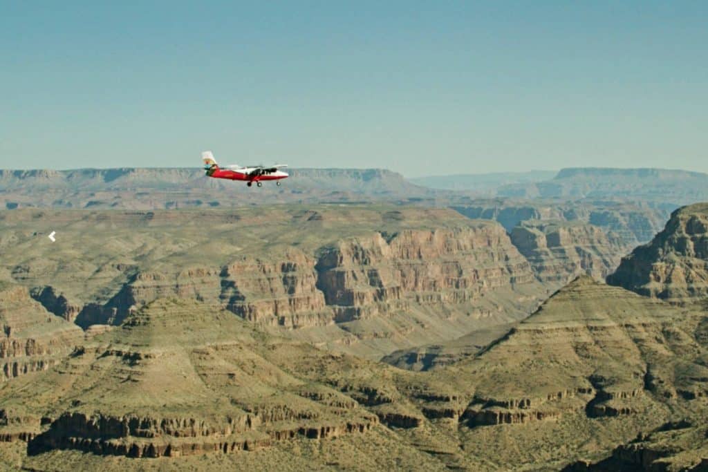 Scenic high-altitude view of a small tour plane flying over the vast, layered plateaus of the Grand Canyon