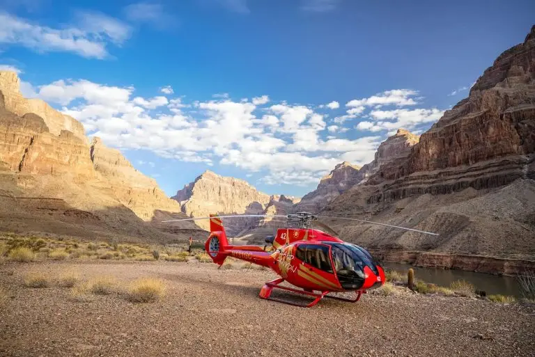 Red tour helicopter landed on a rocky desert floor surrounded by the towering cliffs of the Grand Canyon.