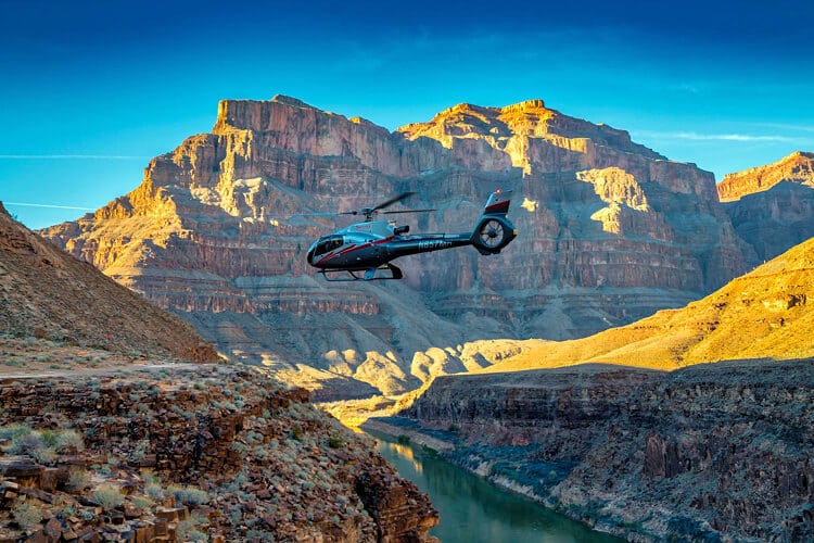 Black tour helicopter flying above the Colorado River between the towering rock formations of the Grand Canyon.